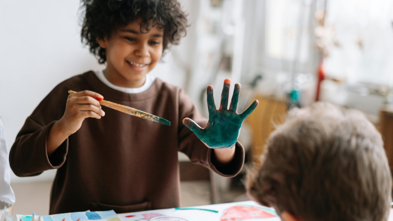 Child showing painted hand to another child indoors