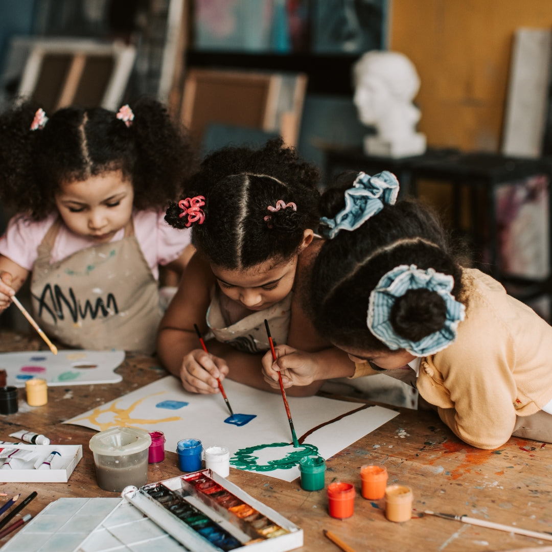 Three children painting at a table with art supplies.