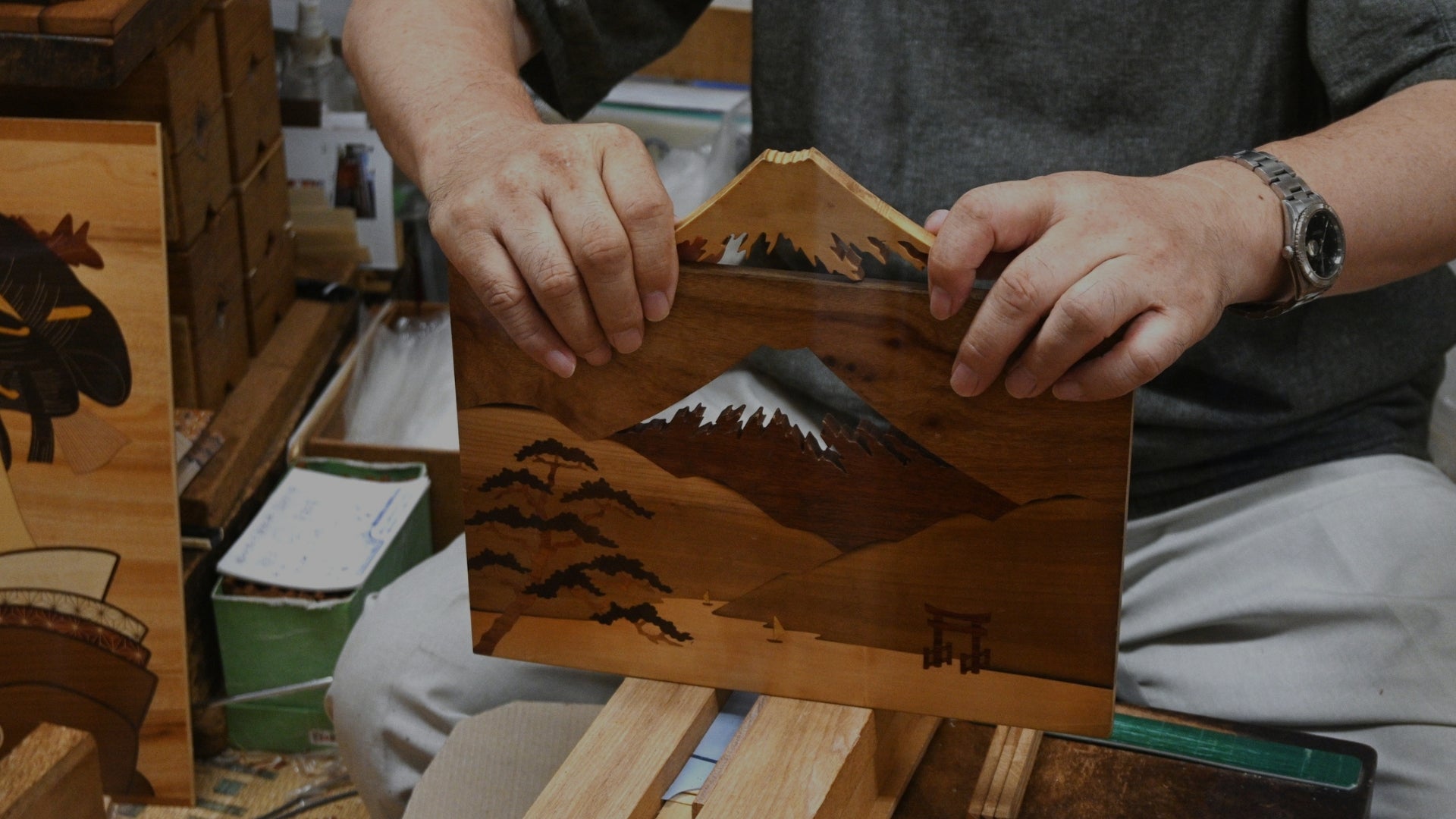 Person holding a wooden panel with mountain design in a workshop setting