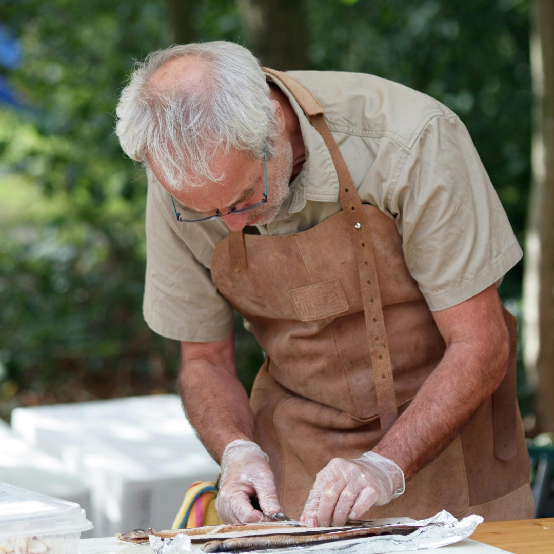 Man in a brown apron and gloves working on food preparation outdoors