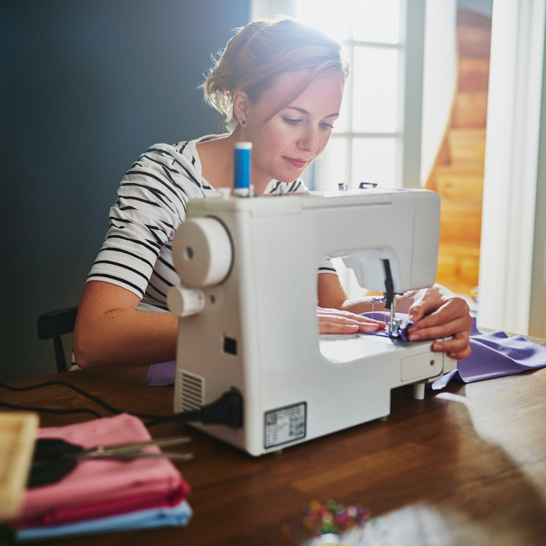 Woman using a sewing machine at a table with a window in the background